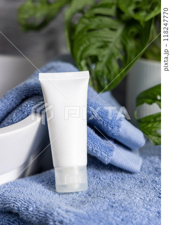 White cream tube on blue folded towel near vessel basin close up in bathroom, cosmetic mockup White cream tube on blue folded towel near vessel basin close up in bathroom, cosmetic mockup 118247770