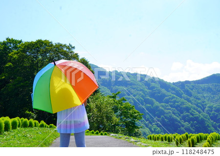 よく晴れた夏の高原でカラフルな日傘をさしている女の子の後ろ姿。 よく晴れた夏の高原でカラフルな日傘をさしている女の子の後ろ姿。 118248475