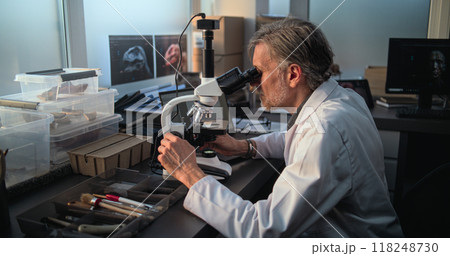 Mature scientist conducts fossil analysis under microscope, uses laptop 118248730