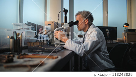 Mature scientist conducts fossil analysis under microscope, uses laptop Mature scientist conducts fossil analysis under microscope, uses laptop 118248829