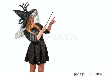 Cheerful young woman in a witch costume happily points with a magic wand, capturing the Halloween spirit Cheerful young woman in a witch costume happily points with a magic wand, capturing the Halloween spirit 118248928