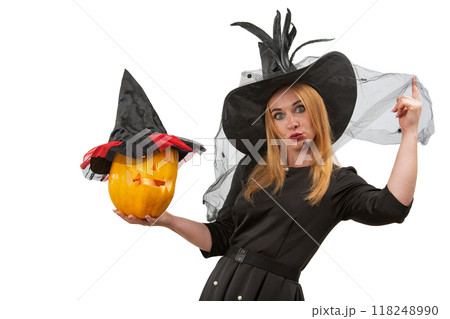 Smiling witch is holding a carved pumpkin wearing a black hat and dress on a white background Smiling witch is holding a carved pumpkin wearing a black hat and dress on a white background 118248990