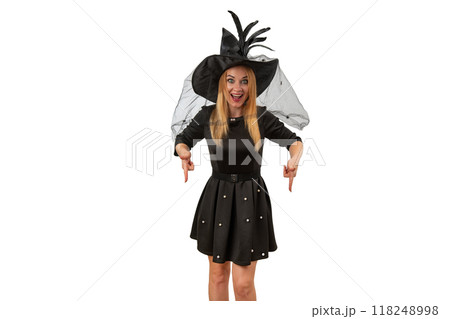 Happy smiling woman in black witch hat and black dress points her fingers down. White background. Mockup. Halloween costume party 118248998
