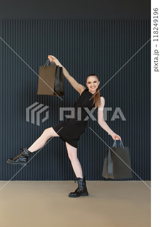 Happy cheerful young woman with black shopping bags takes a long step, seasonal discount. Full length portrait, vertical frame. Black friday, sales Happy cheerful young woman with black shopping bags takes a long step, seasonal discount. Full length portrait, vertical frame. Black friday, sales 118249196