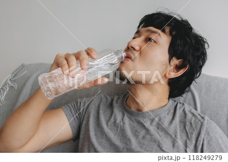 Close up of man sitting on the sofa and drinking bottle of water. 118249279