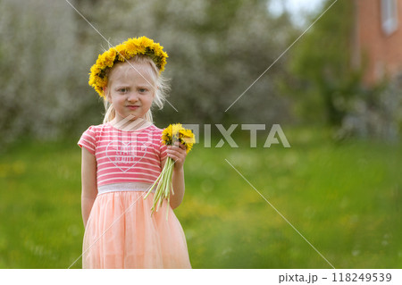Serious blond girl on green field with bouquet of yellow dandelions. Little girl holds flowers, summer day 118249539