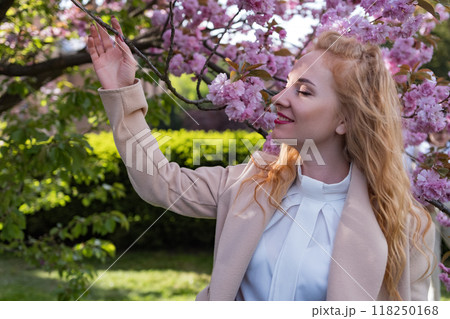 Happy young woman with closed eyes near flowering tree . Portrait of charming fashionable girl in blooming sakura park. Happy young woman with closed eyes near flowering tree . Portrait of charming fashionable girl in blooming sakura park. 118250168