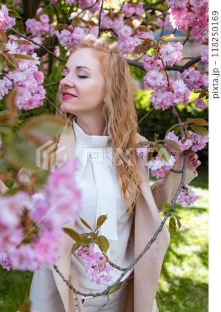 Happy young woman with closed eyes in park among flowering trees . Attractive red-haired girl in blooming park. Vertical frame. Happy young woman with closed eyes in park among flowering trees . Attractive red-haired girl in blooming park. Vertical frame. 118250169