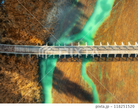 Aerial view of wooden bridge, azure river and orange grass 118251520