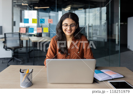 Young beautiful woman working inside office with laptop, business woman typing on keyboard, happy smiling satisfied with work result at workplace, company employee. 118251979