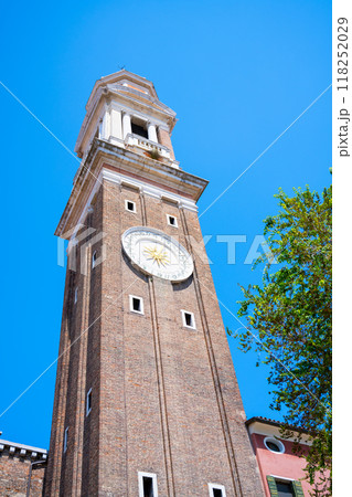 The Campanile dei Santi Apostoli rises 47 meters in the Cannaregio district of Venice, showcasing its historical architecture against a bright blue sky on a sunny day. 118252029