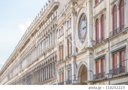 The early Renaissance St Marks Clocktower graces the Piazza San Marco's entrance with its intricate design and colorful clock. Tourists stroll by, enjoying the historic architecture of Venice. 118252223