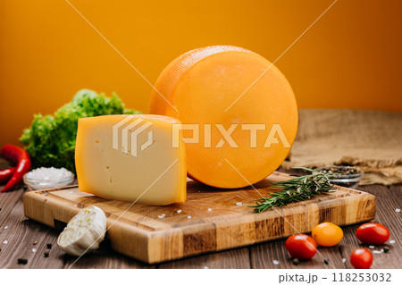 Golden cheese wheel and slice on wooden board, ideal for food photography and culinary presentations Golden cheese wheel and slice on wooden board, ideal for food photography and culinary presentations 118253032