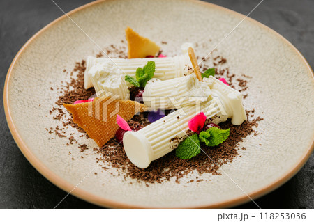 Gourmet dessert with white chocolate, biscuit shards, mint, and edible flowers on a textured plate Gourmet dessert with white chocolate, biscuit shards, mint, and edible flowers on a textured plate 118253036