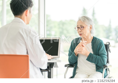 病院・介護施設で医師に病状を伝えるシニア女性と問診する男性医師（診療・診察・人間ドック・健康診断） 118259284