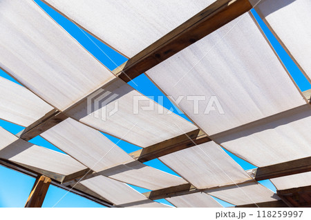 Terrace roof made of strips of white fabric on wooden framework Terrace roof made of strips of white fabric on wooden framework 118259997