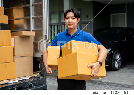 A delivery guy is carrying boxes from his truck to deliver to a customer in front of their house. A delivery guy is carrying boxes from his truck to deliver to a customer in front of their house. 118261635