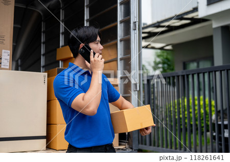 A delivery guy is carrying a package and calling a customer to pick it up in front of their house. 118261641