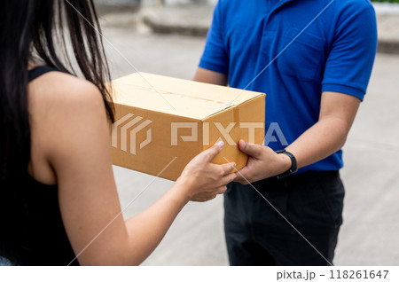 A cropped image of a customer receiving a package from a delivery man in front of her house. 118261647