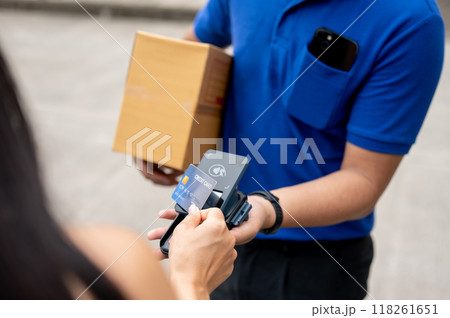 A customer tapping her credit card on a card reader before receiving a package from a delivery man. A customer tapping her credit card on a card reader before receiving a package from a delivery man. 118261651