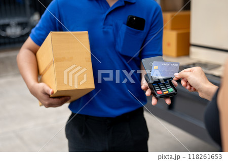 A customer tapping her credit card on a card reader before receiving a package from a delivery man. A customer tapping her credit card on a card reader before receiving a package from a delivery man. 118261653