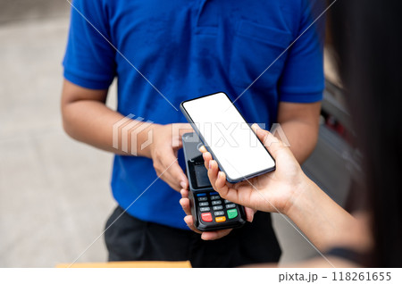 A customer tapping her smartphone on a card reader before receiving a package from a delivery man. A customer tapping her smartphone on a card reader before receiving a package from a delivery man. 118261655