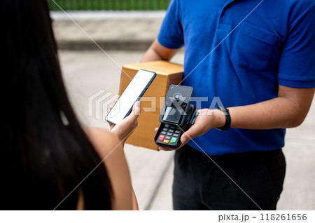 A customer tapping her smartphone on a card reader before receiving a package from a delivery man. A customer tapping her smartphone on a card reader before receiving a package from a delivery man. 118261656