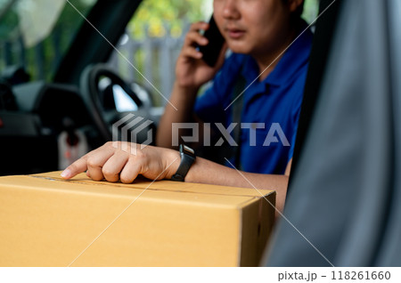 An Asian delivery man is calling a customer from his van before delivering a package. An Asian delivery man is calling a customer from his van before delivering a package. 118261660