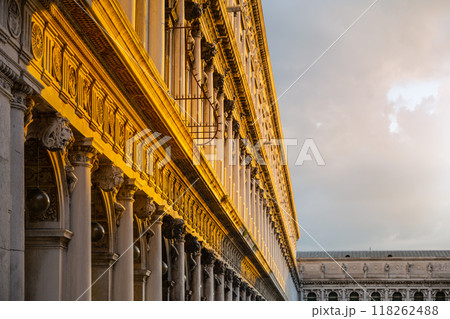 The intricate architectural features of the New Procuracie in Venice are highlighted by the warm glow of the setting sun, showcasing columns and ornate designs against a dramatic sky. The intricate architectural features of the New Procuracie in Venice are highlighted by the warm glow of the setting sun, showcasing columns and ornate designs against a dramatic sky. 118262488
