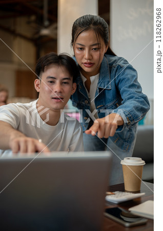 Two Asian friends or colleagues are in a coffee shop, discussing a project while working together. 118262968