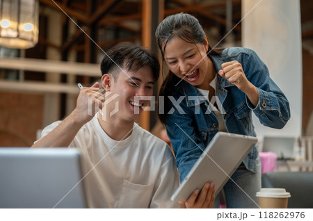 Two cheerful Asian friends are celebrating good news together, looking at a digital tablet. Two cheerful Asian friends are celebrating good news together, looking at a digital tablet. 118262976