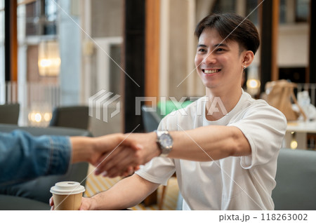 A happy Asian man giving a handshake to his friend during a meeting at a coffee shop. A happy Asian man giving a handshake to his friend during a meeting at a coffee shop. 118263002