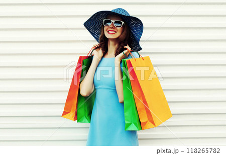 Beautiful happy smiling woman looking at shopping bags in blue dress, summer hat on white background 118265782