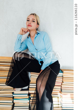 Beautiful blonde woman sitting on stacks of books in library Beautiful blonde woman sitting on stacks of books in library 118266110