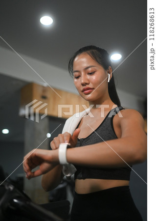 Satisfied female athlete checking her heart rate on smartwatch while exercising in gym. Healthy lifestyle concept Satisfied female athlete checking her heart rate on smartwatch while exercising in gym. Healthy lifestyle concept 118268613