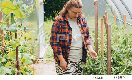 Homemade groceries. Happy blonde woman working on her farm. Young woman in her glasshouse at backyard Homemade groceries. Happy blonde woman working on her farm. Young woman in her glasshouse at backyard 118269769