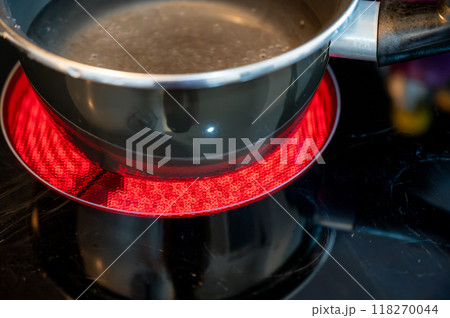 Close-up of a hob with electric hot plates: the heating elements are bright red,the pot of water placed on top is about to boil. Selective focus on the heating elements. Concept of energy consumption 118270044