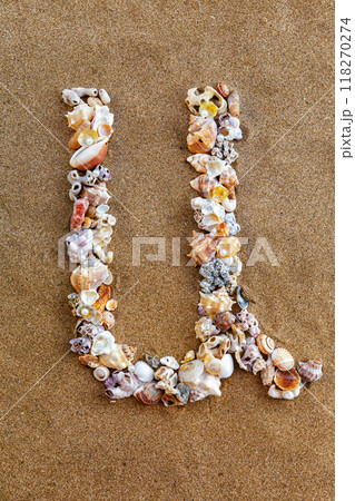 The letter U of the English alphabet, a letter made of seashells on the sand. 118270274