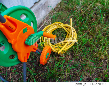 Garden hose reel rests on the grass, next to a neatly coiled yellow hose 118270966