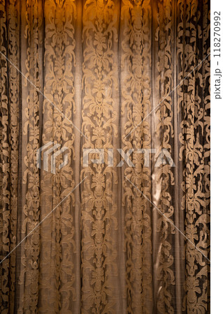 Vintage curtains with a flower pattern, illuminated by the orange light shining through them, create an exciting visual display. Vintage curtains with a flower pattern, illuminated by the orange light shining through them, create an exciting visual display. 118270992