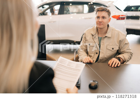 View from shoulder of unrecognizable female manager handing car purchase documents to male buyer to review and sign contract. Man client making agreement with manager. Concept of buying new auto. View from shoulder of unrecognizable female manager handing car purchase documents to male buyer to review and sign contract. Man client making agreement with manager. Concept of buying new auto. 118271318