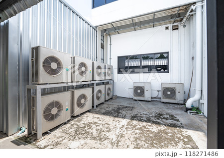 Air conditioning system on ground side of habitat. Multiple white compressor air condition installed in old building.Condenser unit or compressor on ground of building background. Air conditioning system on ground side of habitat. Multiple white compressor air condition installed in old building.Condenser unit or compressor on ground of building background. 118271486