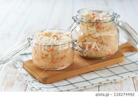 Open glass jar of fermented white cabbage with carrot on a white kitchen table. Open glass jar of fermented white cabbage with carrot on a white kitchen table. 118274492