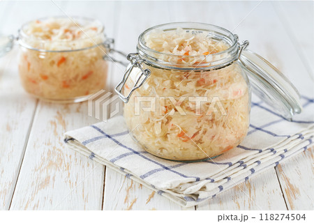 glass storage jar with sauerkraut and carrots on white kitchen table. glass storage jar with sauerkraut and carrots on white kitchen table. 118274504