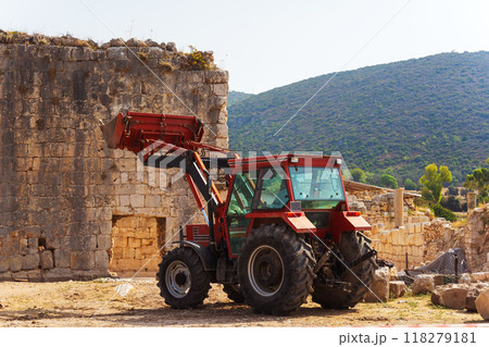 A red tractor is parked in front of a stone building and mountains 118279181