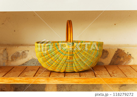 A bright yellow and green woven basket is resting on a wooden shelf A bright yellow and green woven basket is resting on a wooden shelf 118279272