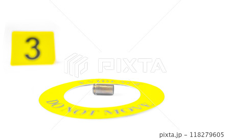 A spent bullet casing placed within a yellow circle, labeled with the text "Evidence, Do Not Move," with a blurred number 3 tag, set against a white background, concept of crime investigation. 118279605