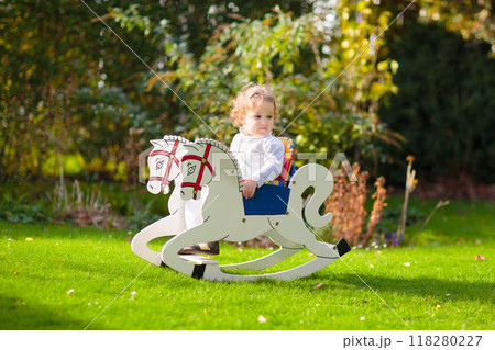 Little girl on rocking horse in summer garden Little girl on rocking horse in summer garden 118280227