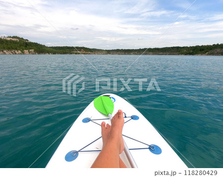 Girl on a SUP board floating on the surface of the blue water of a quarry lake with rocky shores and trees growing on them on a summer day. Summer sports, tourism, recreation, relaxation, travel, rest 118280429