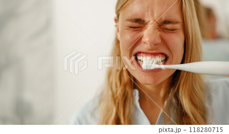 A woman is brushing her teeth with an electric toothbrush in a modernstyle bathroom space A woman is brushing her teeth with an electric toothbrush in a modernstyle bathroom space 118280715